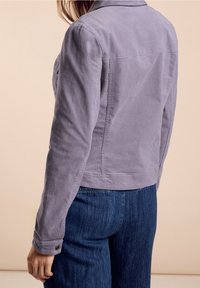 Lila kordjacka med krage, knappade ärmslut och en figursydd design. Bärs över denimjeans som visar ett texturerat tyg.