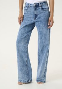 Ljust blå denimjeans med vid benvidd och en något slitna yta, prydda med glittrande dekorationer på framsidan. Hög midja.