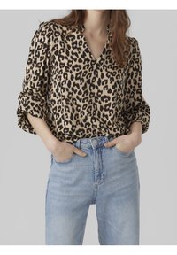 Leopardmönstrad blus i beige och svart, med v-ringning och puffärmar, kombinerad med högmidjade ljusblå jeans. Mjuk tygtextur.