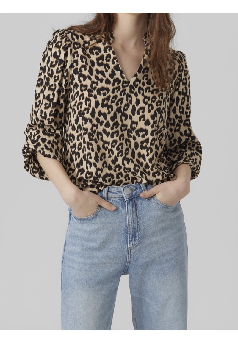 Leopardmönstrad blus i beige och svart, med v-ringning och puffärmar, kombinerad med högmidjade ljusblå jeans. Mjuk tygtextur.