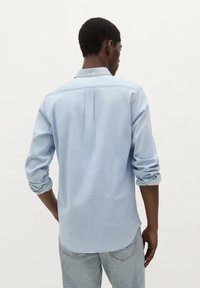 Lichtblauw shirt met lange mouwen, geknoopte kraag en een enkele rugplooi; zachte stof en opgerolde mouwen onthullen een casual ontwerp.