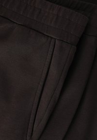 Donkerbruine broeken met een gladde textuur, uitgerust met een brede tailleband en geplooide details aan de voorkant, gestikt met contrasterende draad.