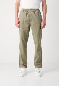 Helle khakifarbene Freizeit-Hosen mit elastischem Bund, Fronttaschen und lockerer Passform, kombiniert mit weißen Sneakern. Minimalistisches Design.