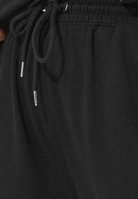 Svarta sweatpants med elastiskt midjeband, dragsko med metallspetsar och en mjuk, slät textur.