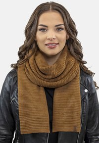 Hnědý strukturovaný pletený šátek, širokého obdélníkového tvaru, s žebrovaným vzorem. Nesený přes černou koženou bundu.