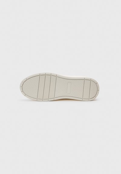 Schuhsohle von unten betrachtet, hellbeige mit strukturiertem Grip-Muster aus Quadraten und horizontalen Rillen auf einem schlichten weißen Hintergrund.