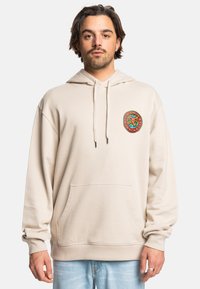 Béžová mikina vyrobená z mäkkej látky, s predným vreckom a farebnou kruhovou grafikou na ľavej hrudi. Kapucňa na šnúrku a ribbované manžety.