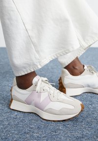 Les baskets présentent une combinaison de cuir blanc, d'accents rose clair, de panneaux en daim et d'une semelle en caoutchouc texturé. Les lacets sont d'une teinte neutre.
