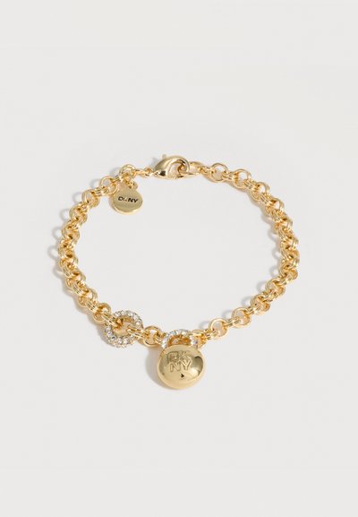 Bracelet chaîne en or avec fermoir mousqueton, comportant deux charms ronds, l'un gravé "DKNY" et l'autre avec des strass clairs.
