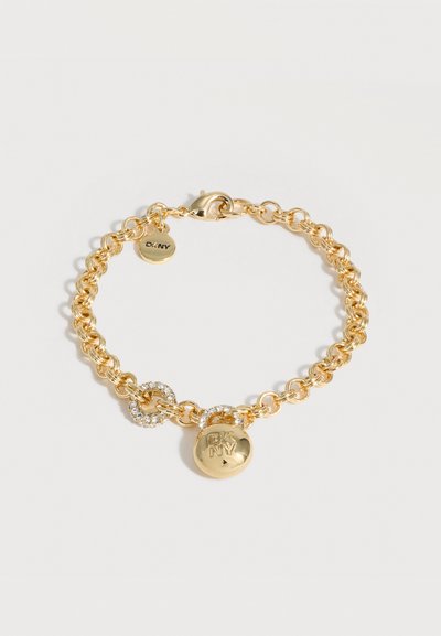 Bracelet chaîne en or avec fermoir mousqueton, comportant deux charms ronds, l'un gravé "DKNY" et l'autre avec des strass clairs.