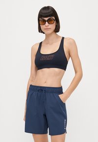 Melna sporta krūšturis ar sarkanu "ROXY" logotipu. Gaisīgas jūras zila šorti ar elastīgu jostasvietu un sānu kabatām. Gluda, ātri žūstoša auduma.