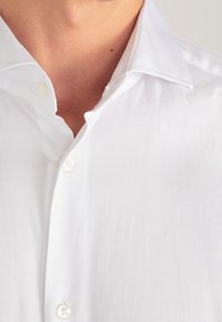 Camisa blanca de vestir con cuello clásico, cierre frontal con botones y textura suave. Presenta botones pequeños y redondos y un diseño limpio.