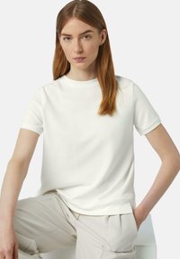 White short-sleeve t-shirt made of cotton with a round neckline and minimal design. Worn with light-colored, loose-fitting trousers.