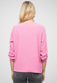 Maglietta rosa a maniche lunghe con polsini arrotolati, vestibilità ampia, scollatura rotonda e texture morbida, abbinata a pantaloni in denim grigi.