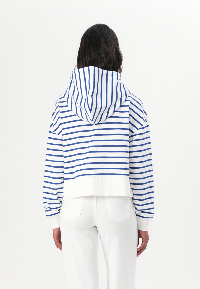 Pasiasta, krótsza bluza z kapturem w białym i niebieskim kolorze, z luźnym krojem, ściągaczami przy rękawach oraz gładkim, białym dołem.