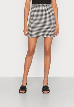Mini-jupe en vichy noir et blanc avec un design ajusté, associée à des sandales à glissière tissées noires, mettant en valeur un matériau texturé et des lignes épurées.