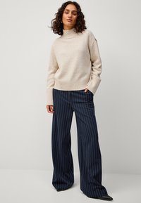 Beige coltrui met geribde zoom, gecombineerd met marineblauwe gestreepte wijde broek. Grote kleurcontrast, zachte textuur en een getailleerde pasvorm.
