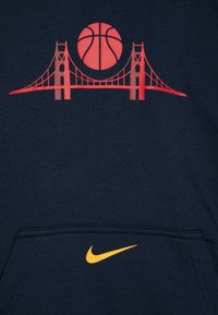 Mornarska dukserica s crvenim grafičkim prikazom mosta i košarkaške lopte, uz žuti Nike logo na dzepu. Mekani materijal, klasičan kroj.