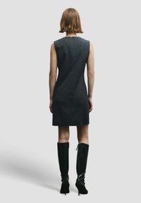 Vestito nero senza maniche con texture a costine, lunghezza al ginocchio, con collo alto e cerniera nascosta sul retro. Abbinato a stivali neri al ginocchio.