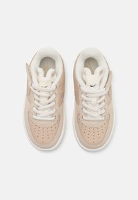 Nike-sneakers i ljusbeige läder med perforerade detaljer, vita snören och plyschiga, kaninformade tunga-accenter. Mjuk innertyg.