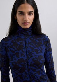 Camicia a collo alto aderente blu e nera con motivo, realizzata in tessuto elastico, con chiusura a zip e maniche lunghe con dettagli di cucitura sottili.