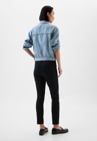 Világoskék farmerdzseki felhajtott ujjakkal és két hátsó zsebbel, fekete szűk nadrággal és fekete mokaszinokkal párosítva. Egyszínű háttér.