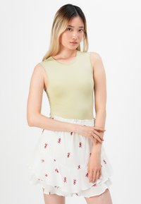 Bodysuit sin mangas de color verde claro combinado con una falda blanca de capas que presenta patrones de flores bordadas en rojo. Diseño minimalista, textura suave.