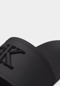 Μαύρο σανδάλι χωρίς λουράκια με ανάγλυφο λογότυπο "CK" στο φαρδύ άνω λουρί, λείο υλικό και εργονομική σόλα.