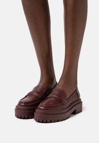 Mocasines de cuero burdeos con suela elevada, presentan una puntera cosida, detalle de tira ancha y suela de goma texturizada.