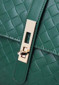 Borsa a tracolla in pelle intrecciata verde con finitura liscia, dotata di una chiusura in tonalità oro e dettagli hardware rettangolari. Design strutturato, senza motivi.