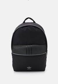 Black backpack with a rounded shape, featuring a mesh front pocket, three vertical stripe accents, and a silver logo at the base.