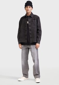 Grijze spijkerjasje met een enkele voorzak over een zwart T-shirt, gecombineerd met lichtgrijze baggy jeans en witte sneakers.