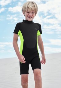 Rövid neoprén ruha fekete anyagból, élénk neonzöld oldalpanelekkel. Sima textúra, rövid ujjú, hátul cipzáros záródással.