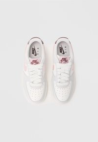 Bijele i svijetlo sive Nike Air Force 1 tenisice imaju ružičaste akcentne boje, okrugli vrh, perforirani gornji dio i bijele vezice. Logo se nalazi na jeziku i sa strane.