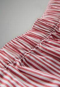 Tessuto a righe rosse e bianche con una textura arricciata e dettagli di cucitura sottili, che mette in mostra un morbido materiale di cotone in una vista ravvicinata.