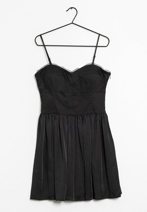 Vestido negro sin mangas con borde de encaje en el busto, cuerpo ajustado y falda plisada colgado en una percha de alambre negra sobre un fondo blanco.