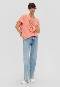 Rosa kurzärmliges Oberteil kombiniert mit hellblauen Schlagjeans und weißen Sneakers. Das Oberteil hat eine lockere Passform und ein schlichtes Design.