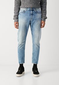 Jeans en denim bleu clair avec une finition délavée, coupe droite et design à cinq poches, associés à des baskets en daim noir.