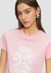 Helles rosa Baumwoll-T-Shirt mit einem weißen Blumenmotiv und Textdesign. Runder Ausschnitt und kurze Ärmel. Glatte Textur.