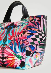 Sac fourre-tout coloré à motif tropical avec des poignées en cuir synthétique noir, présentant des designs floraux vibrants en tons de rose, bleu et vert.