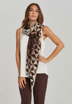 Écharpe aux motifs marron et beige en triangles géométriques, fabriquée en tissu doux avec bords effilochés, portée drapée sur un haut blanc.