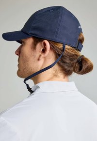 Cappello blu navy realizzato in tessuto testurizzato, con visiera curva e cinturino regolabile. La parte posteriore presenta una cinghia per il mento per una vestibilità sicura.