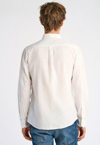 Witte linnen blouse met lange mouwen, slim fit, met een rugplooi en knoopmanchetten, gecombineerd met blauwe jeans.