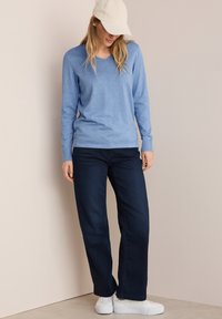 Ljusblå långärmad tröja med v-ringning, ihop med mörkblå vida jeans och vita sneakers. Personen bär också en krämfärgad basebollkeps.