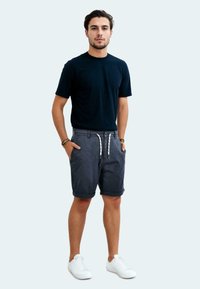 Marineblaues T-Shirt mit kurzen Ärmeln, kombiniert mit grauen Shorts mit Kordelzug. Getragen mit weißen Sneakers, ist der Look lässig und komfortabel.