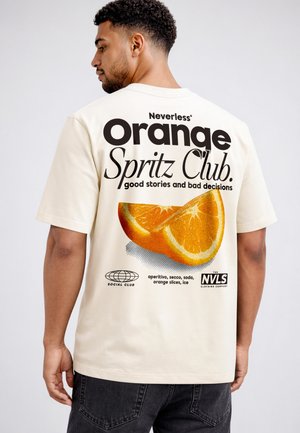 Man wearing cream shirt with large orange slices and text "Orange Spritz Club, good stories and bad decisions" on back.