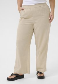 Pantaloni beige leggeri a gamba larga con cintura elastica, dotati di tasche laterali e tessuto texture. Abbinati a sandali flip-flop neri.