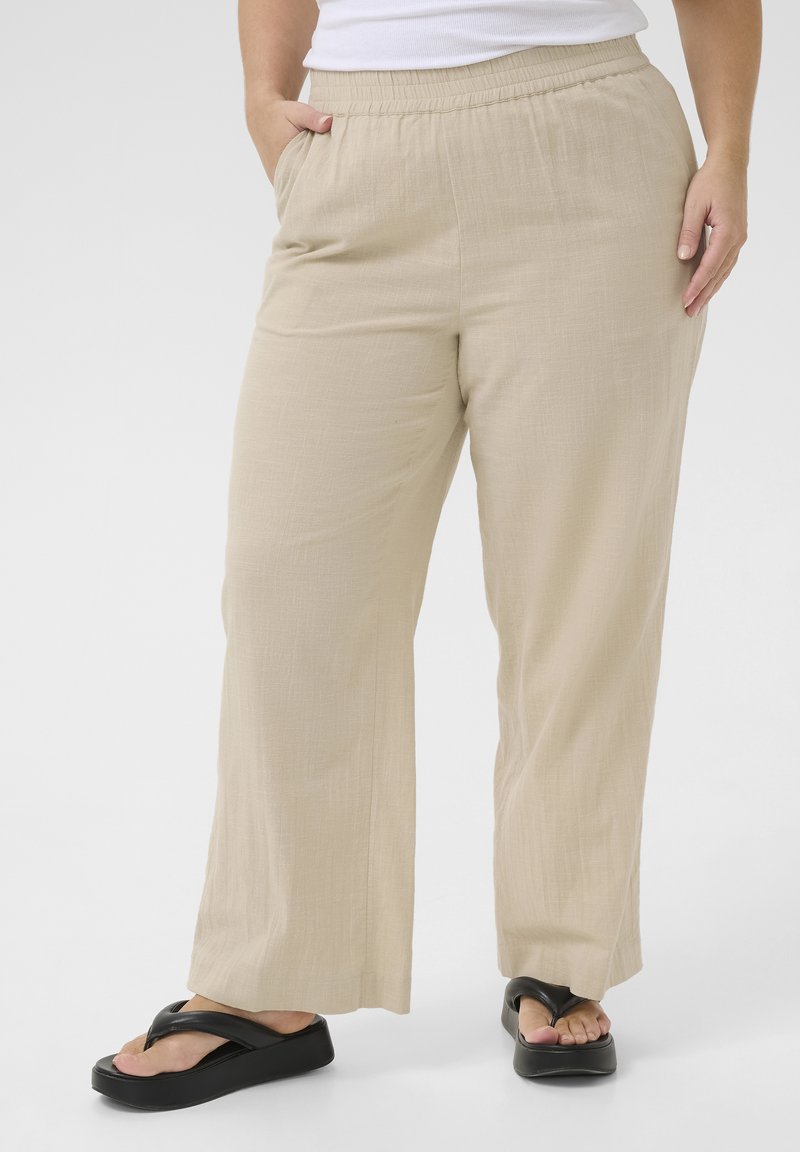 Pantaloni beige leggeri a gamba larga con cintura elastica, dotati di tasche laterali e tessuto texture. Abbinati a sandali flip-flop neri.