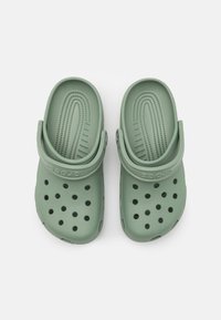 Zeleni gumijasti klobuki z ventilacijskimi luknjami, teksturirano vložkom, nastavljivim trakom za peto in blagovno znamko Crocs na strani.