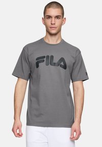 Camiseta de algodón gris con un gran logo negro de FILA en el frente, de mangas cortas y con diseño de cuello redondo.